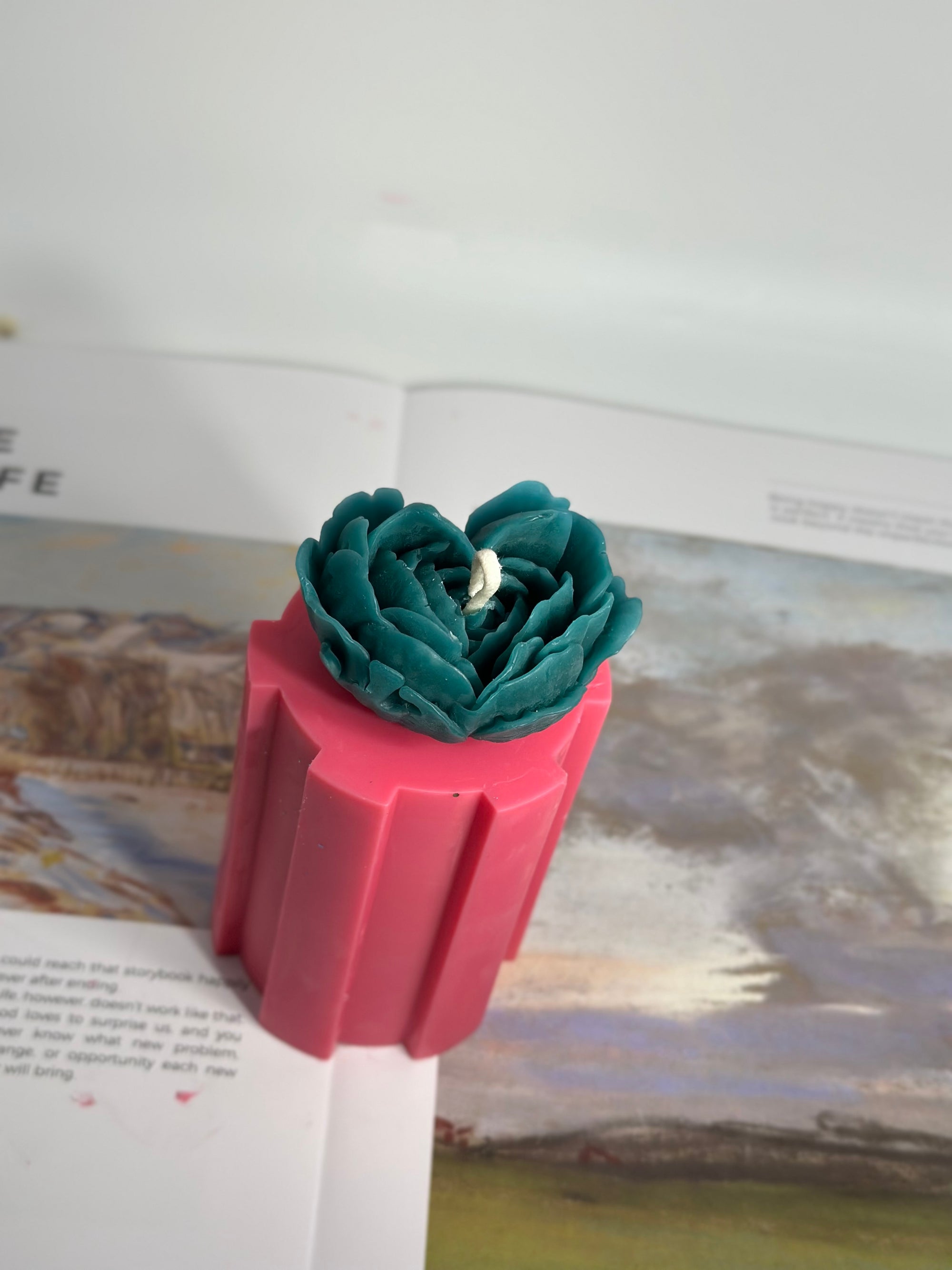 Vue latérale d'une bougie en cire végétale, détails sculptés de la fleur turquoise sur base rose. Fait main à Paris.